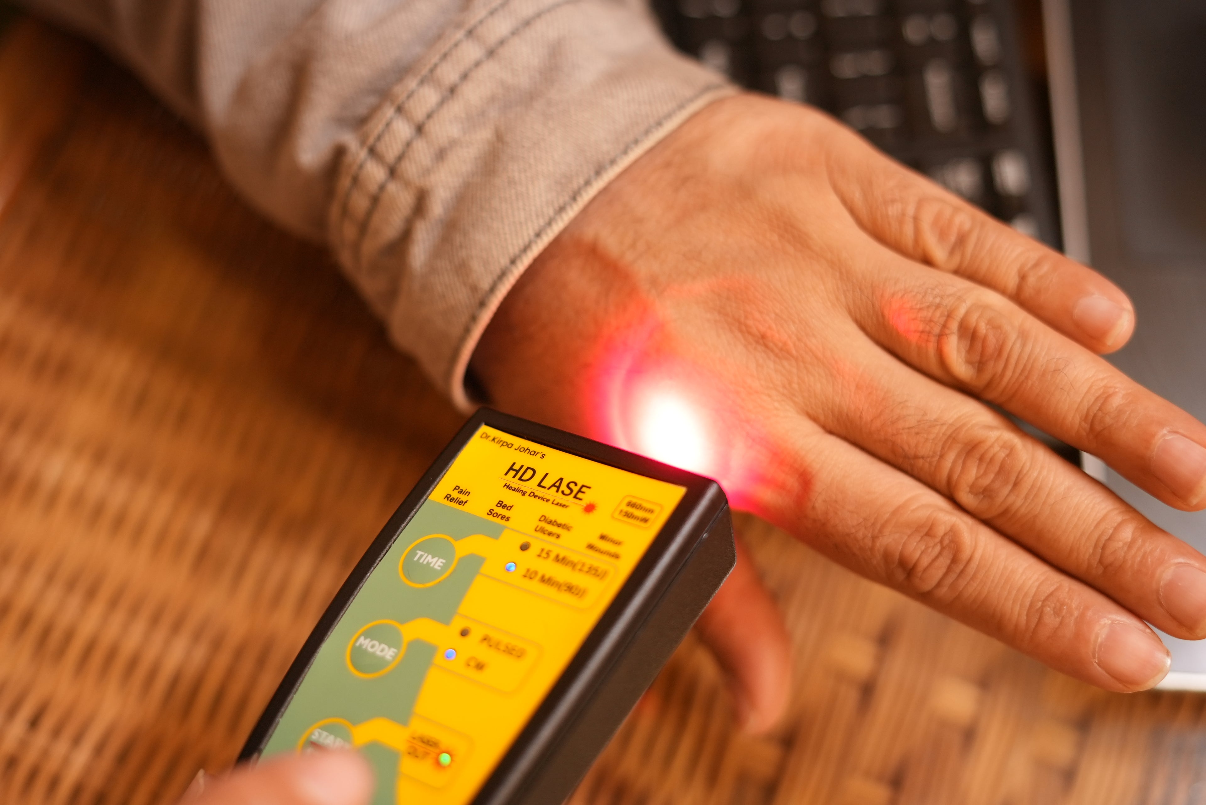 Handheld device emitting a red laser onto a hand with a blurred background